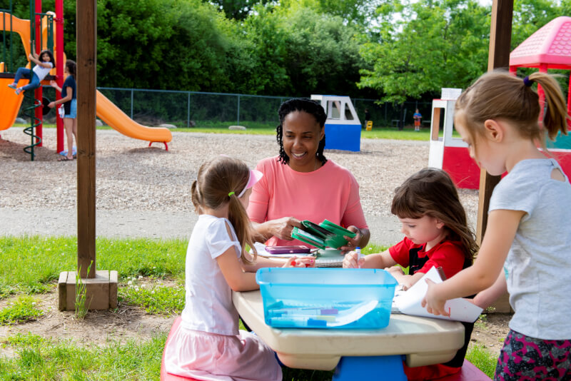 A teacher guides an activity outside with children.