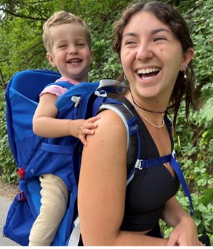 Hackman carries a young child on her back, both smiling. 