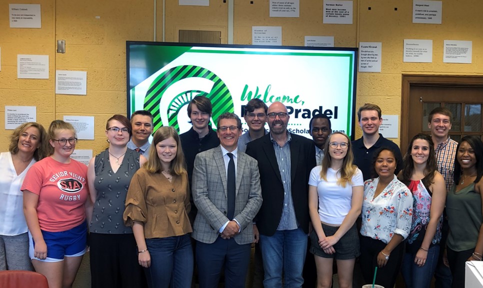 Paul Pradel smiles with a group of  about 15 students in a classroom.