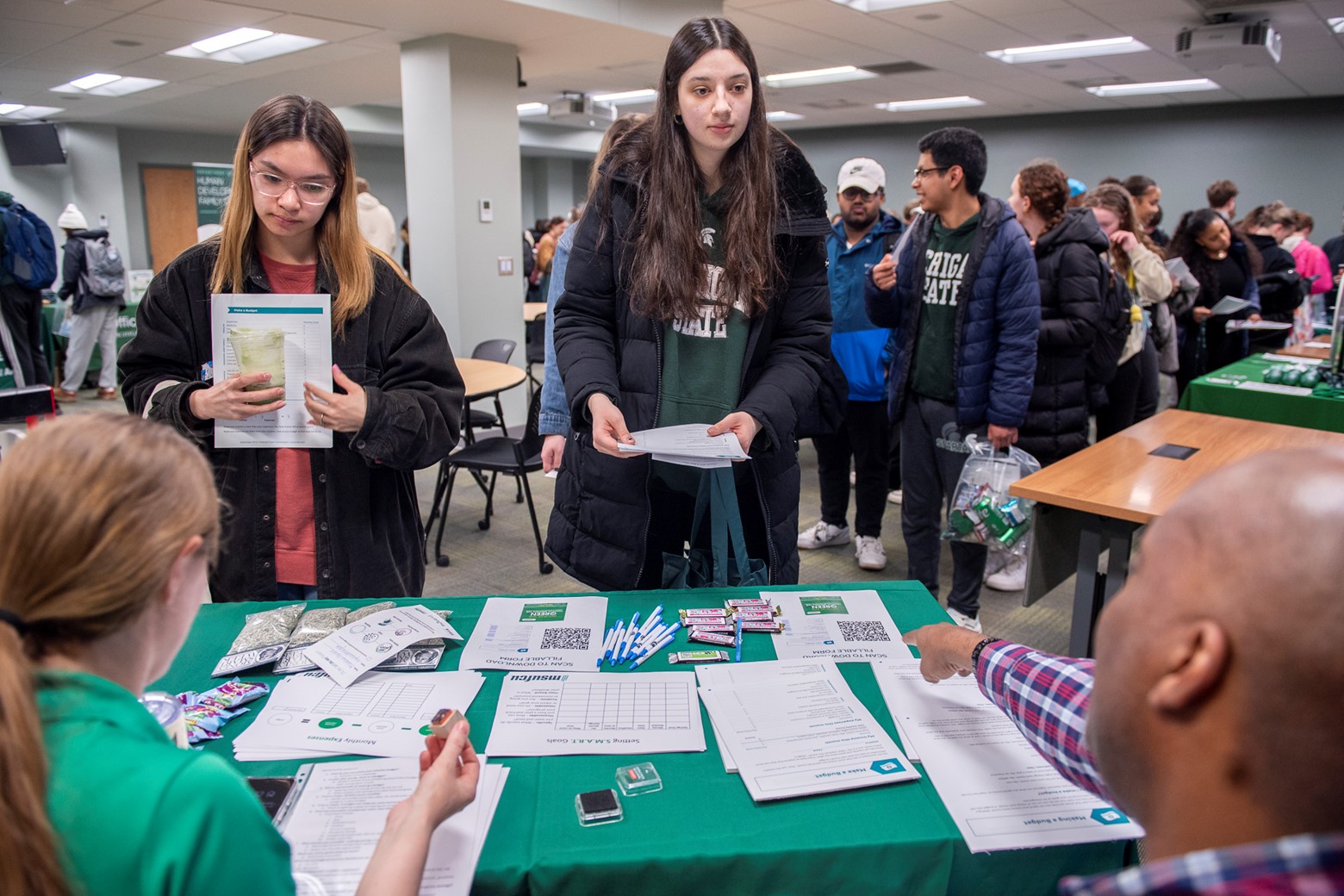 Male and female students stand around a booth listening to the financial literacy representatives. 